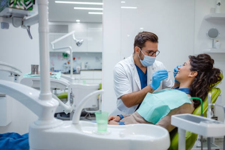 A dental professional is examining the oral health of a patient seated in a modern dental chair within a well-equipped dental clinic